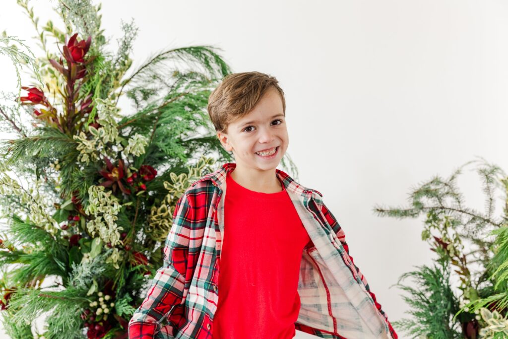 KId photographed against a botanical holiday greenery background.