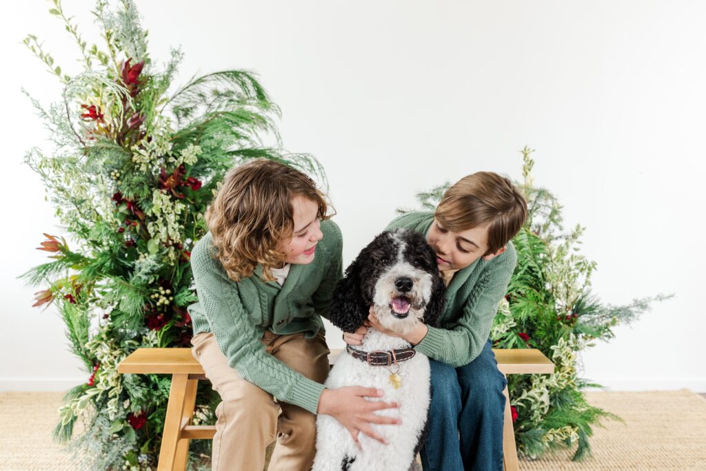 Two kids with their pet in a Holiday greenery background