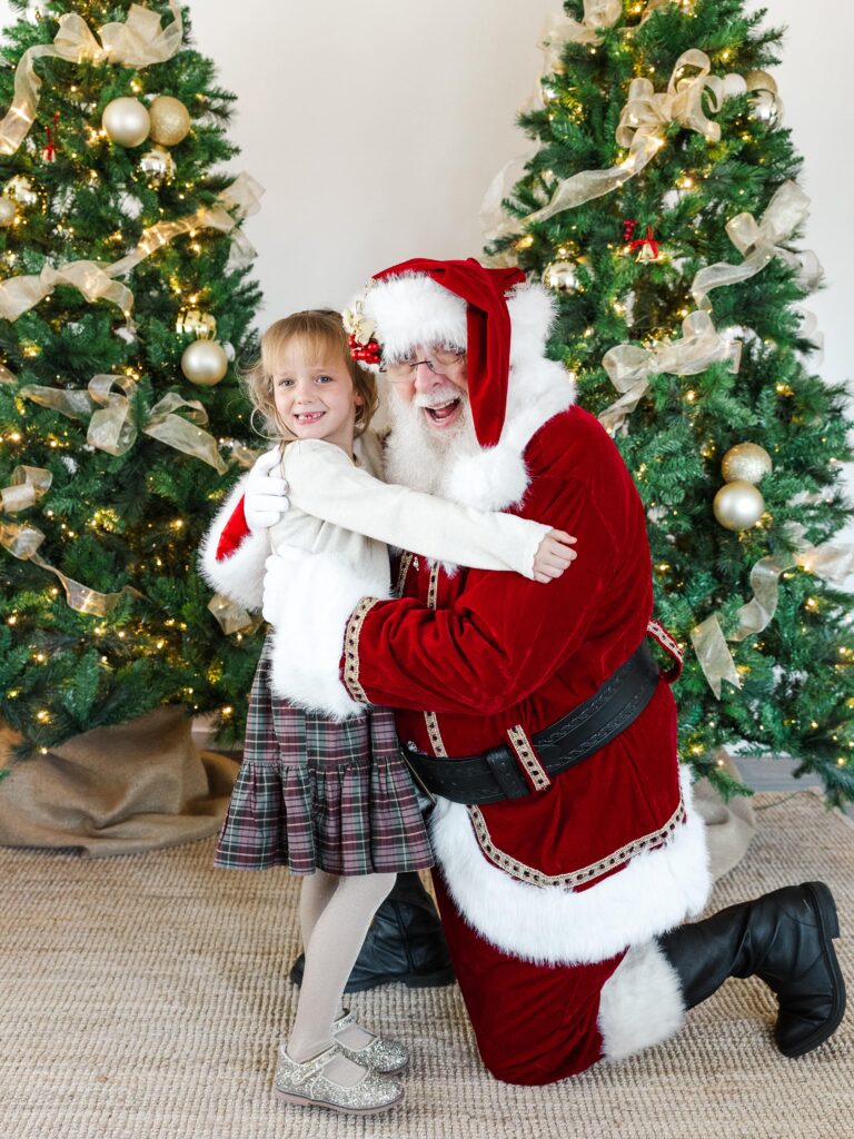 Little girl hugging and smiling with Santa during Holiday Kids Portrait  session.