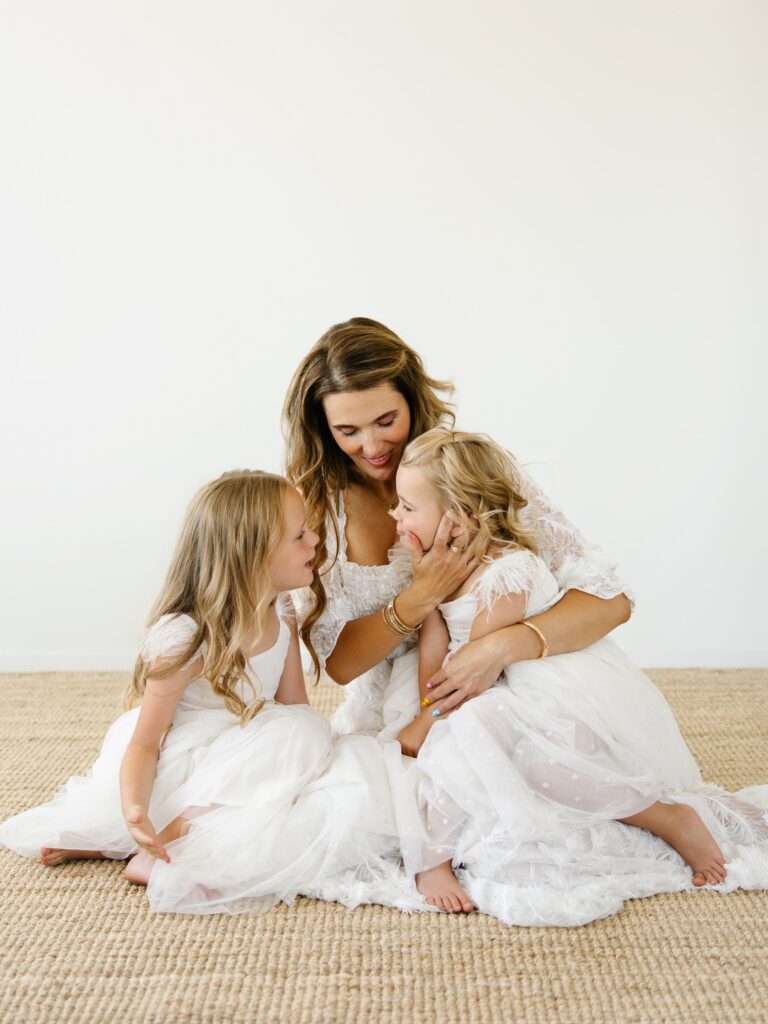 Amara and her daughters smiling together during a styled indoor motherhood session, soft natural light.