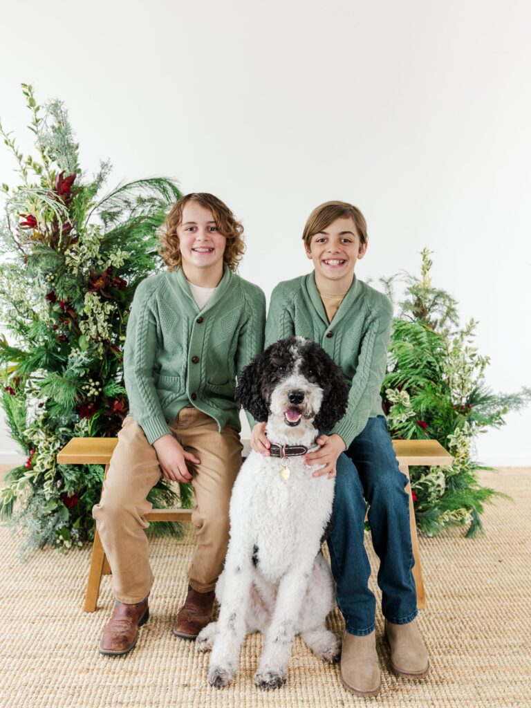 Kids smiling in front of a holiday greenery backdrop during a festive portrait session.
