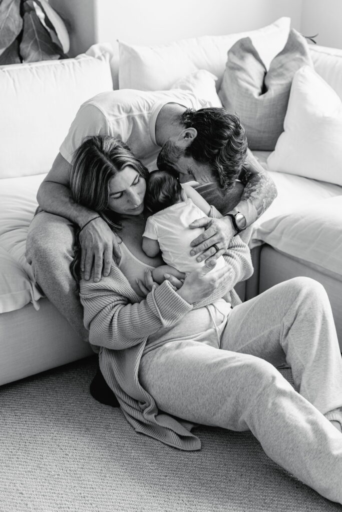 Family gathered around their baby in a bright, peaceful living room.
