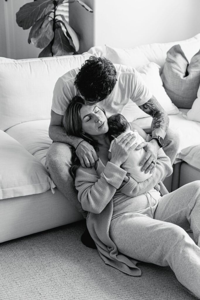 Family snuggling on the couch with their newborn in natural light.
