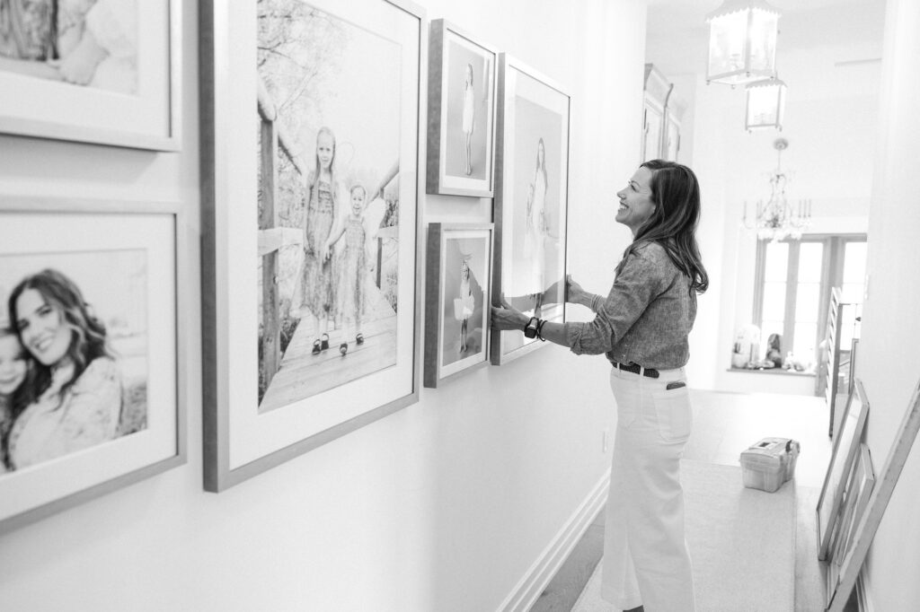 Photographer adjusting a black and white framed portrait in a hallway gallery wall
