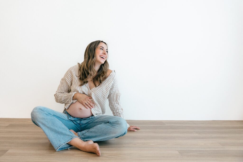 Pregnant mother standing in a white shirt and jeans during a studio maternity session